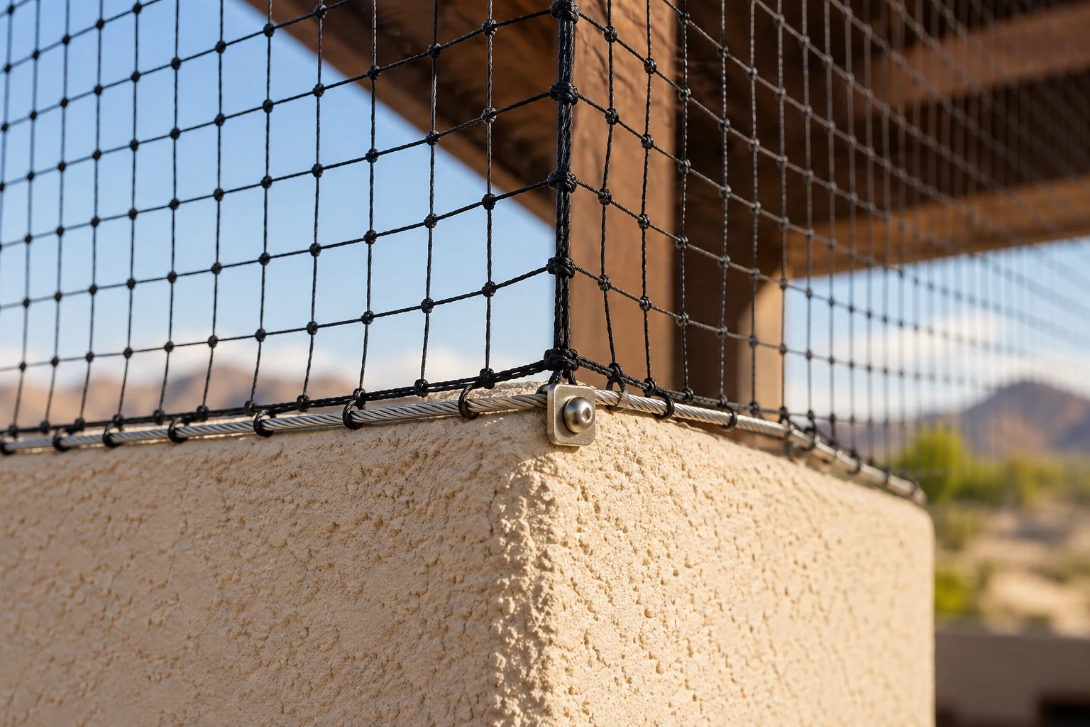 Black knotted bird netting secured along a perimeter cable at a stucco corner